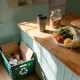 A keep cup, a jar of pantry staples and a produce bag of fruit and vegetables on a kitchen bench beside an open recycling crate in an Australian home.