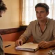 A GP going through paperwork with a patient over a timber desk in a warm Australian consultation room.