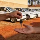 A staff member's hand passing a set of car keys to a customer at a car rental lot lined with white cars in an Australian town.