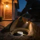 A homeowner lifting the lid of a water meter pit and shining a torch inside at dusk beside an Australian brick home.