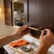 Two hands fitting a brass bar handle to a dark timber cabinet door with a screwdriver, tools resting on the bench below.