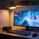 A night desk setup with a monitor glowing a blurred game scene, a mechanical keyboard, headset and a plain PC tower with a subtle internal light.